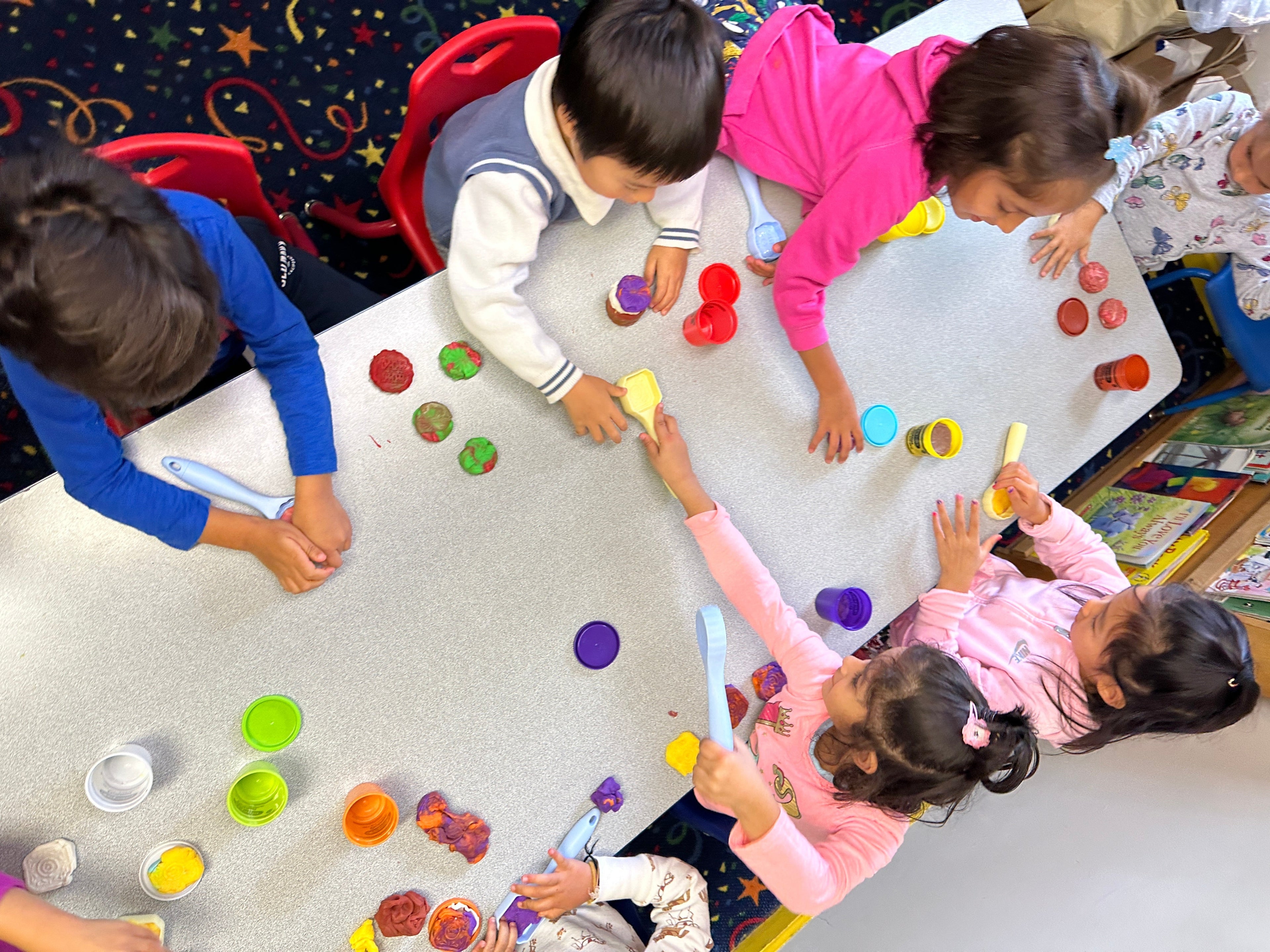 Children playing with colorful toys at a table in a classroom setting.